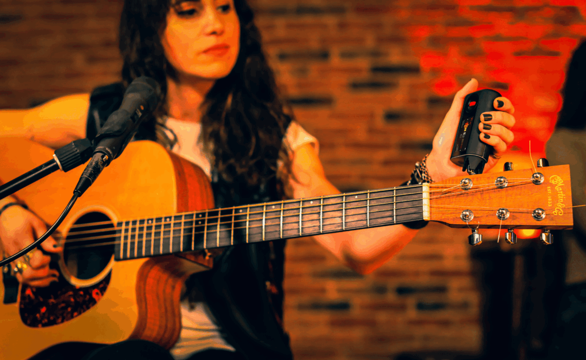 Musician tuning an acoustic guitar using the Roadie 4 automatic tuner during a live performance.