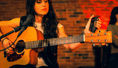 Musician tuning an acoustic guitar using the Roadie 4 automatic tuner during a live performance.