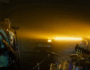 A band performing on a small stage with warm yellow backlighting, featuring a smiling guitarist singing into a microphone, a drummer in the background, and dramatic stage lighting creating depth