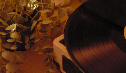 A vinyl record spinning on a turntable next to a plant in warm ambient lighting.