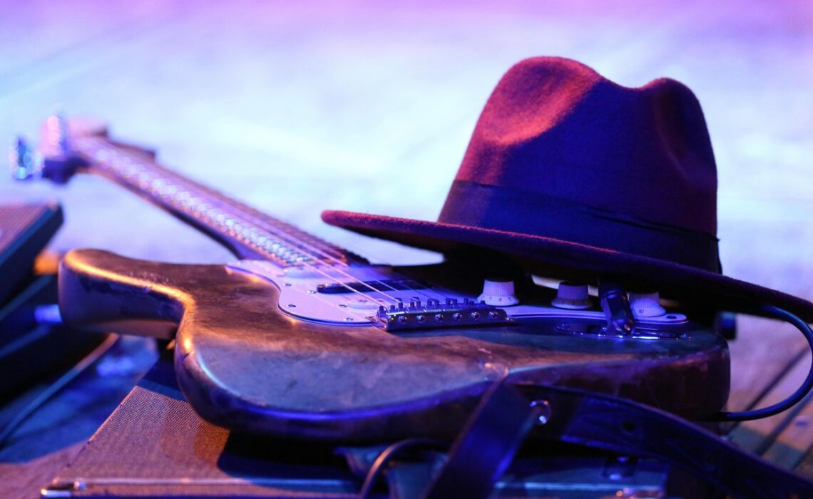 Mississippi Delta Blues guitar resting on stage with hat under colorful concert lights