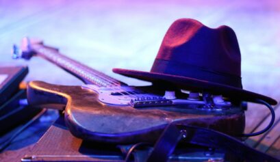Mississippi Delta Blues guitar resting on stage with hat under colorful concert lights