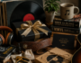 Unique gifts for music lovers displayed on a wooden table, featuring vinyl records, headphones, a guitar, handmade accessories, books, and wrapped gift boxes.