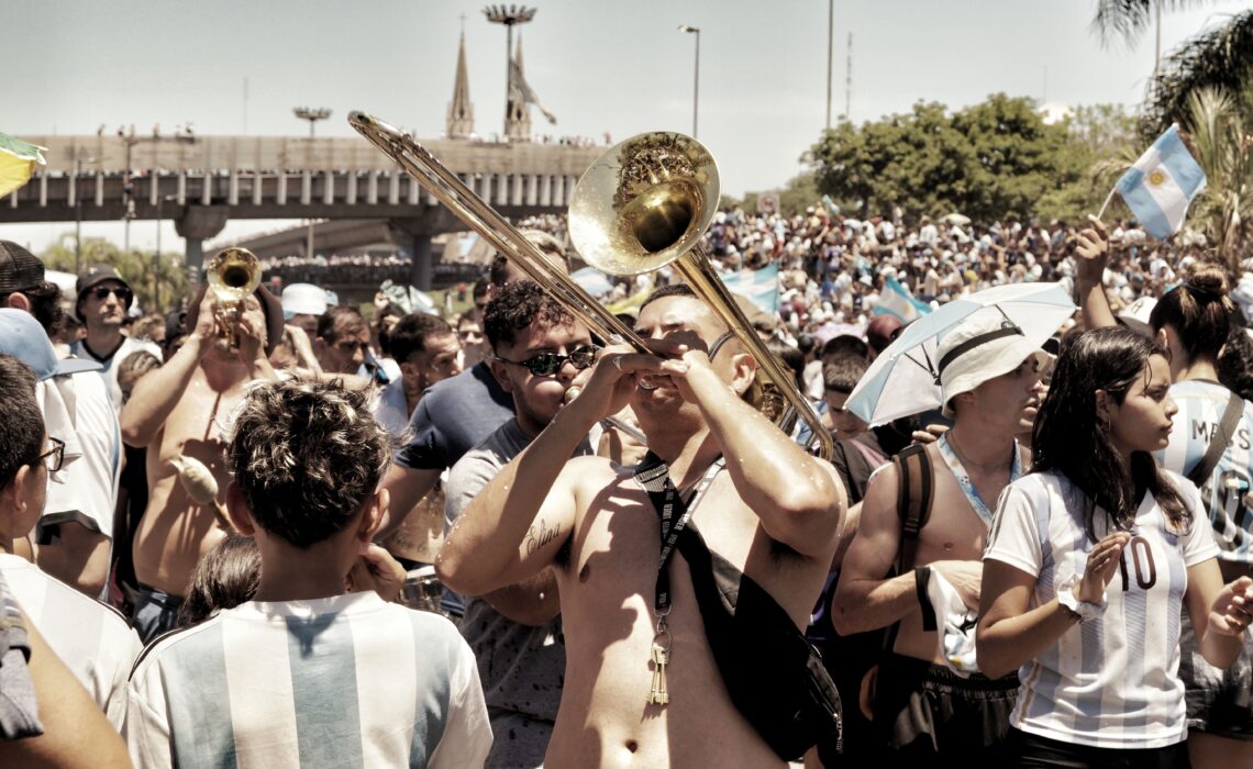 Argentina supporters playing brass instruments and singing during a football celebration, highlighting the role of music in football culture.