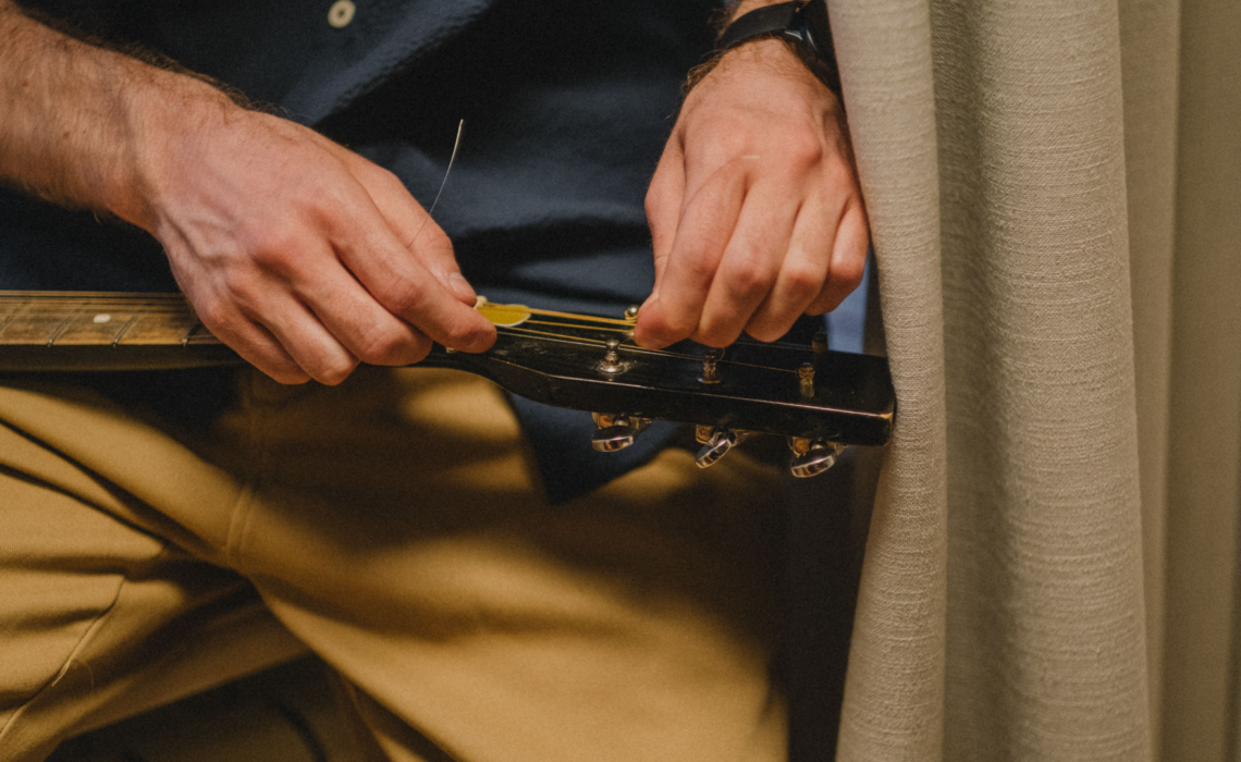 Musician replacing guitar strings while tuning an acoustic guitar.