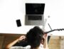 Guitarist practicing acoustic guitar at home beside a laptop, surrounded by everyday music and practice essentials.